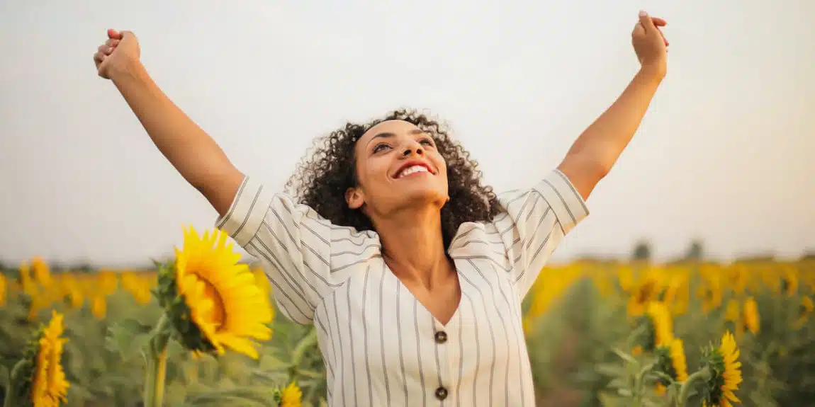 happy woman standing with raised hands in field